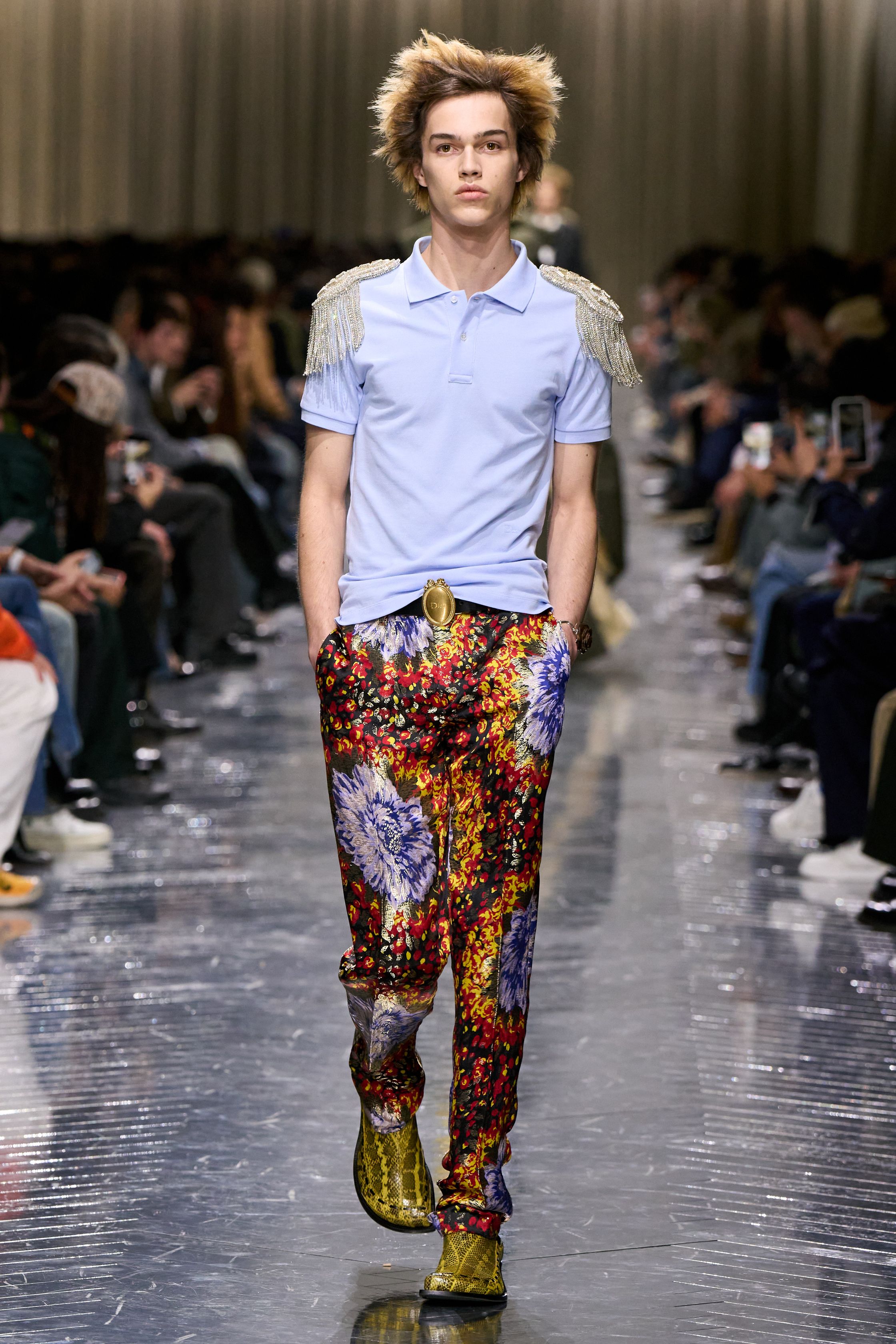 本季 Dior Men 2026 秋冬在克制与叛逆之间建立起新的男性气质坐标。轮廓上，柔软针织、披风式外套与军装结构形成张力对照，模糊正装与休闲、性别与功能的边界；材质层面，羊毛、皮革、毛绒与轻量技术面料并置，强化“触感叙事”。色彩从学院派的灰蓝、橄榄绿过渡至点状印花与手工肌理，传递一种被精心编排的随性。整体呈现出一种“新贵游牧者”形象：既有高级定制的工艺根基，又拥抱当代青年对自由、混搭与身份流动性的渴望-顽石频道趋势研究